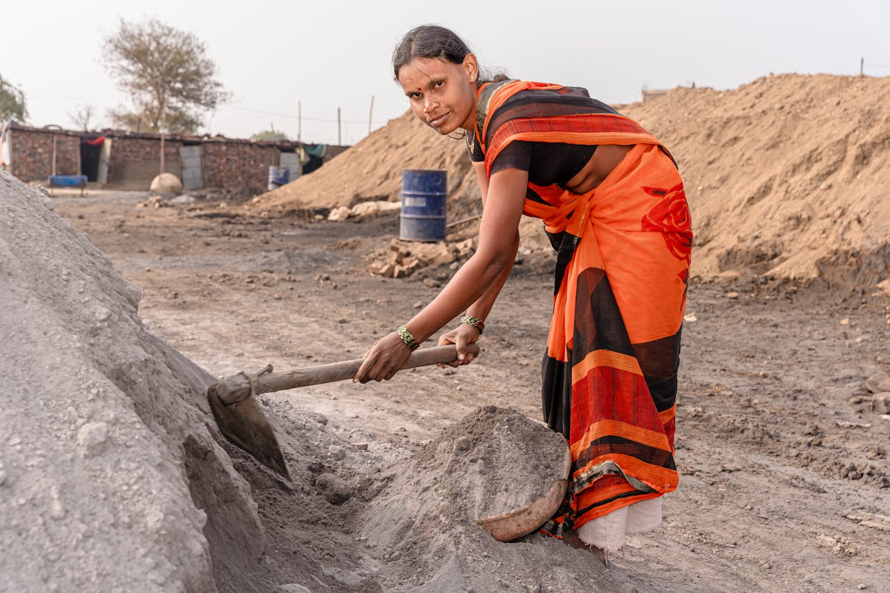 Woman in traditional attire working with a shovel in a rural setting.